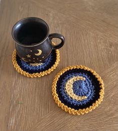 two crocheted coasters sitting on top of a wooden table next to a coffee cup