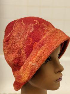 This hat is red with orange and yellow.  It is a cross between a beanie and a cloche style hat.  I made this from merino wool roving, with silk and pieces of yarn all felted to a single, seamless piece.  I love the warm colors reminiscent of a sunset.  In addition to the warm colors, the hat itself will keep one warm on a chilly day or evening. The hat was made using a wet felting process which involves laying out the roving and other fibers and then manipulating while it is wet and soapy by hand for several hours before finally shaping it and letting it dry for a day. This is one of a kind, wearable art.  It would make a perfect gift for someone who loves unique accessories. Red Brimmed Felt Hat For Winter, Red Wool Winter Hat, Red Adjustable Winter Felt Hat, Red Wool Felt Hat With Curved Brim, Red Wool Felt Hat For Winter, Orange Brimmed Hat For Fall, Fitted Red Wool Hat, Red Wool Brimmed Hat, Orange Hat With Short Brim, One Size Fits Most