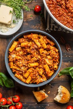 pasta with meat and tomatoes in a bowl on a wooden table next to other ingredients