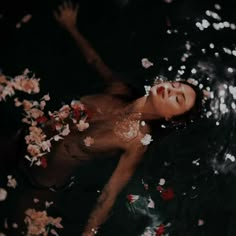 a woman is floating in the water with flowers all around her and looking up at something