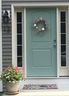 a blue front door with a potted plant next to it and a wreath on the side