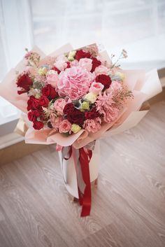 a bouquet of red and pink flowers sitting on top of a wooden floor next to a window