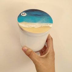 a person holding up a cup with an ocean scene on the top and sand in the bottom