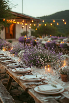 an outdoor dinner table set up with plates and place settings, lit by string lights