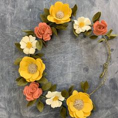 paper flowers arranged in the shape of a circle on a gray surface with green leaves