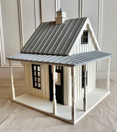 a model house with a metal roof and white sidings on the front door, sitting on a beige carpeted floor