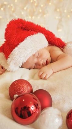 a baby wearing a santa hat sleeping next to christmas ornaments