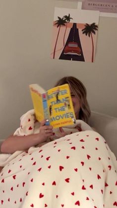 a woman laying in bed reading a book with her head turned to the side while holding a teddy bear