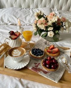 a tray topped with pastries and fruit on top of a bed next to a cup of coffee