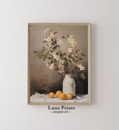 a white vase filled with flowers and oranges on top of a table next to a wall