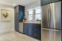 a kitchen with blue cabinets and stainless steel refrigerator freezer combo in the center, along with hardwood flooring