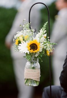 sunflowers and daisies in a mason jar tied to a black metal stand