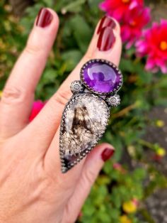 A beautiful, bold talon ring, completely handmade from recycled sterling silver. It holds a deep purple amethyst that seems to glow in the light, and a delicately patterned plume agate stone, with a subtle shimmer and hint of purple. A gorgeous match of stones, this ring is a real statement piece! It sits on a wide, adjustable ring band. All metal is eco solid sterling silver and fine silver and it has been oxidised for a dark, and slightly gothic finish. Purple Jewelry With Natural Inclusions For A Gift, One Of A Kind Amethyst Jewelry, Unique One-of-a-kind Amethyst Jewelry, One Of A Kind Silver Amethyst Jewelry, Purple Gemstone Fusion Rings, Unique Purple Cabochon Jewelry, Mystical Amethyst Ring In Sterling Silver, Unique Adjustable Amethyst Ring In Sterling Silver, Adjustable Sterling Silver Amethyst Ring