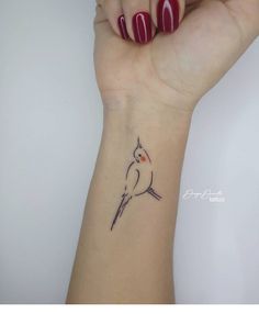 a small bird tattoo on the wrist is shown in black ink and red nail polish