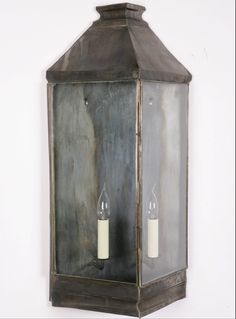 two candles are lit in an old - fashioned metal lantern hanging on the wall,