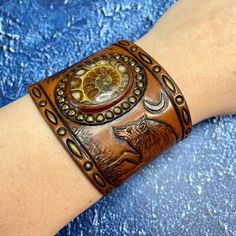 a woman's arm with a brown leather bracelet and an intricate design on it