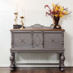 an old dresser with flowers and candles on top is displayed in front of a white wall