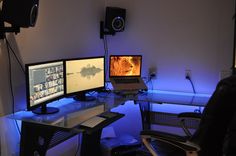 three computer monitors sitting on top of a glass desk