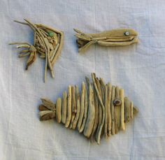 three pieces of driftwood are arranged on a white tablecloth, one is shaped like a fish and the other is made out of sticks