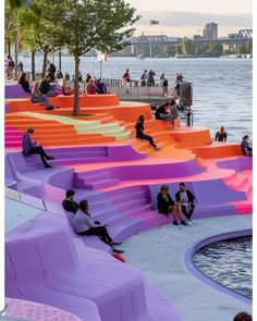 people are sitting on colorful benches by the water