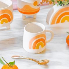 an orange and white coffee cup sitting on top of a table next to two spoons