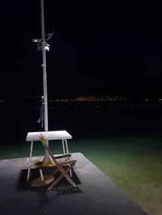 a white table and chair sitting on top of a wooden pier at night with city lights in the background