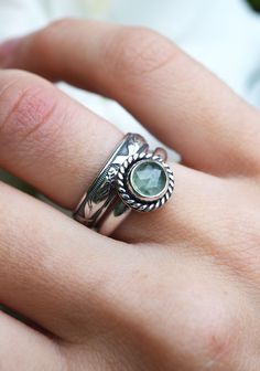 a close up of a person's hand wearing a silver ring with a green stone