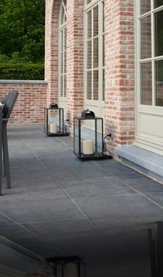 two black lanterns sitting on top of a cement floor next to a brick building with windows