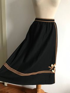 Vintage 70's a-line tailored skirt in good quality medium weight black gaberdine wool with suede / faux suede trimming. Striking geometric line detail going across the bottom of the skirt, the waistband and along the side in a coffee-caramel shade of suede or faux suede fabric. Abstract / floral appliqué design on one side near the bottom.  Back zipper opening secured by hook & eye. Fully lined inside & hidden pockets at each side at hip height. Wide A-line model in a very chic and sophisticated Retro Black A-line Skirt, Black A-line Retro Skirt, Black Retro A-line Skirt, Vintage Knee-length Brown Skirt, Vintage Brown Knee-length Skirt, Retro Brown Flared Skirt, Retro Black Long Skirt, Vintage Black Lined Skirt, Retro Brown Skirt