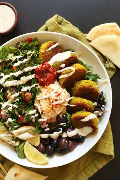 a white bowl filled with food next to some pita bread and dipping sauce on top of it