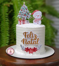 a white cake decorated with a snowman and a christmas tree on top that says feliz natak