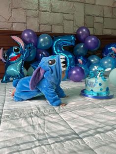 a birthday cake and decorations on a bed with balloons in the shape of characters from stitch