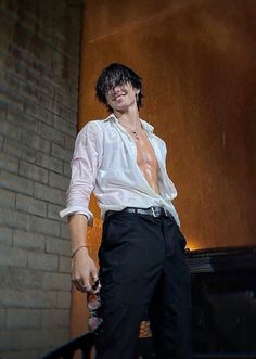 a man in white shirt and black pants standing next to brick wall