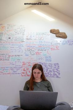 a woman sitting in front of a laptop computer with writing on the wall behind her