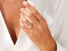 a close up of a person wearing a white shirt holding a ring with a diamond on it