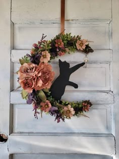 a wreath with flowers and a cat hanging on the front door to decorate it for halloween