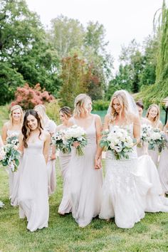 a bride and her bridals walking in the grass at their wedding ceremony with bouquets