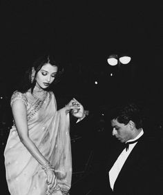 a black and white photo of a woman in a sari standing next to a man