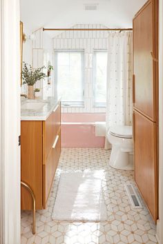 a bathroom with pink and white tile, wood cabinets, and a toilet