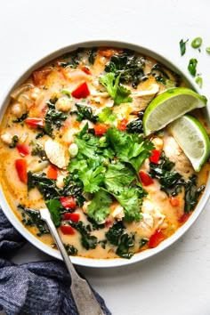 a white bowl filled with chicken, spinach and red peppers next to a lime wedge