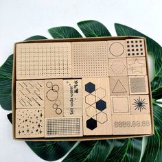 a wooden box filled with lots of different types of shapes and sizes on top of a green leaf