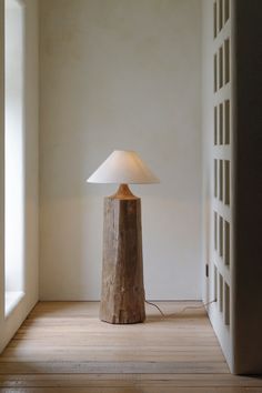 a wooden table lamp sitting on top of a hard wood floor next to a white wall