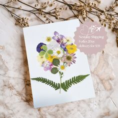 a card with flowers on it sitting next to some dried plants and twigs in the background