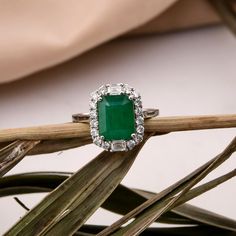 an emerald and diamond ring sitting on top of a plant