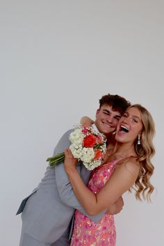 a man and woman hugging each other in front of a white wall