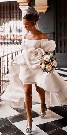 a woman in a white dress is walking down the street wearing high heels and holding a bouquet