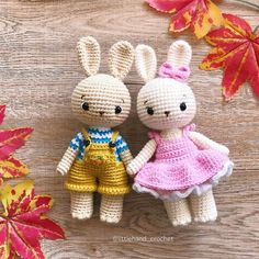 two crocheted rabbits are standing next to each other on a wooden surface with autumn leaves