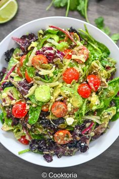 a salad with tomatoes, lettuce and avocado in a white bowl