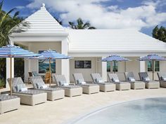 an outdoor pool with lounge chairs and umbrellas next to the side of the swimming pool