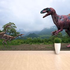 three dinosaurs are walking in the grass near a white cup on a wooden table with mountains in the background